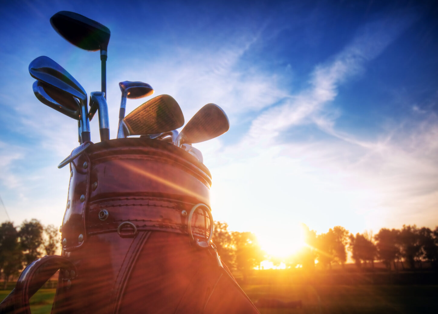 Golf clubs in a golf bag at sunset.