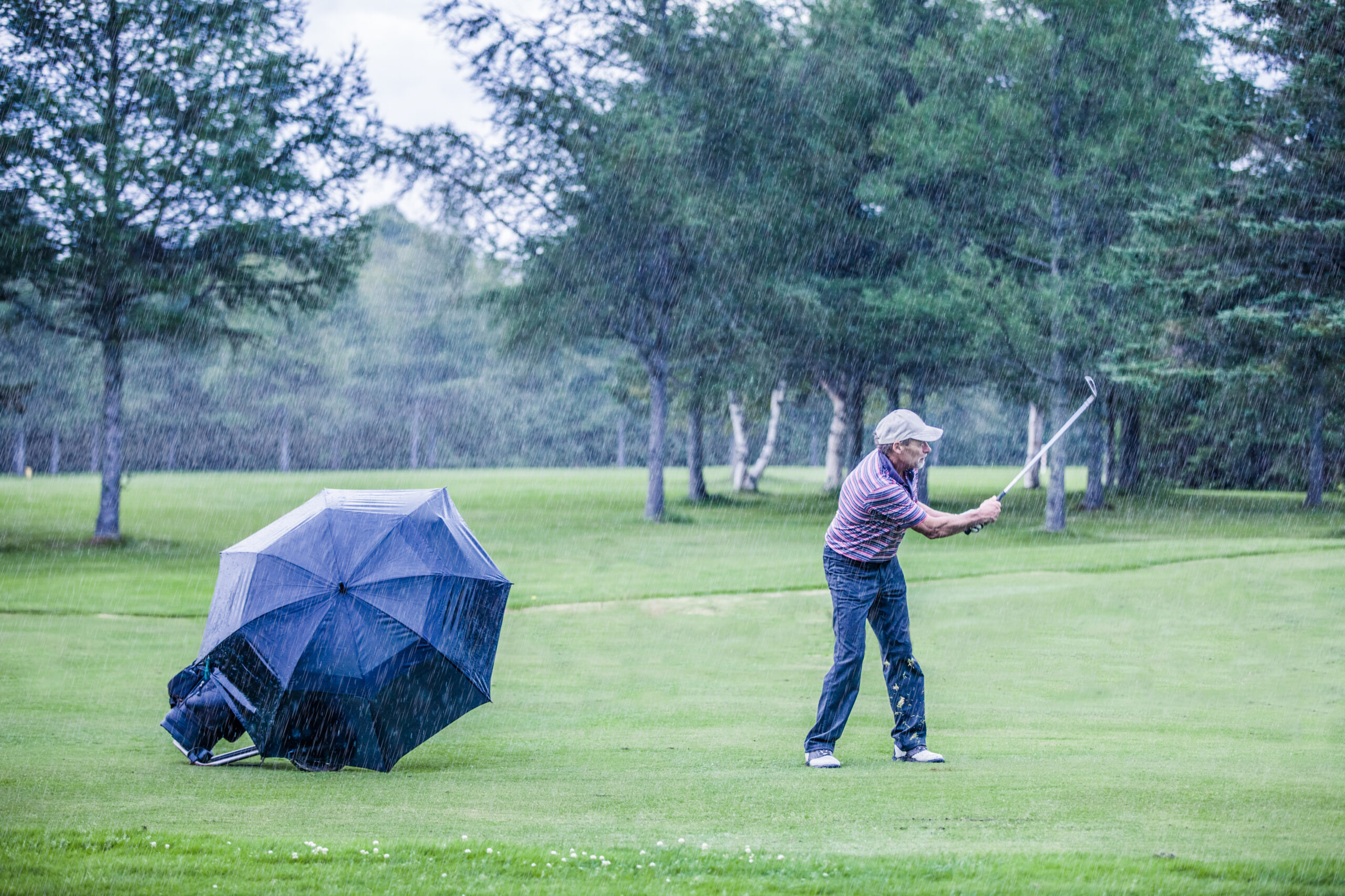 A golfer hits a golf shot in the rain.