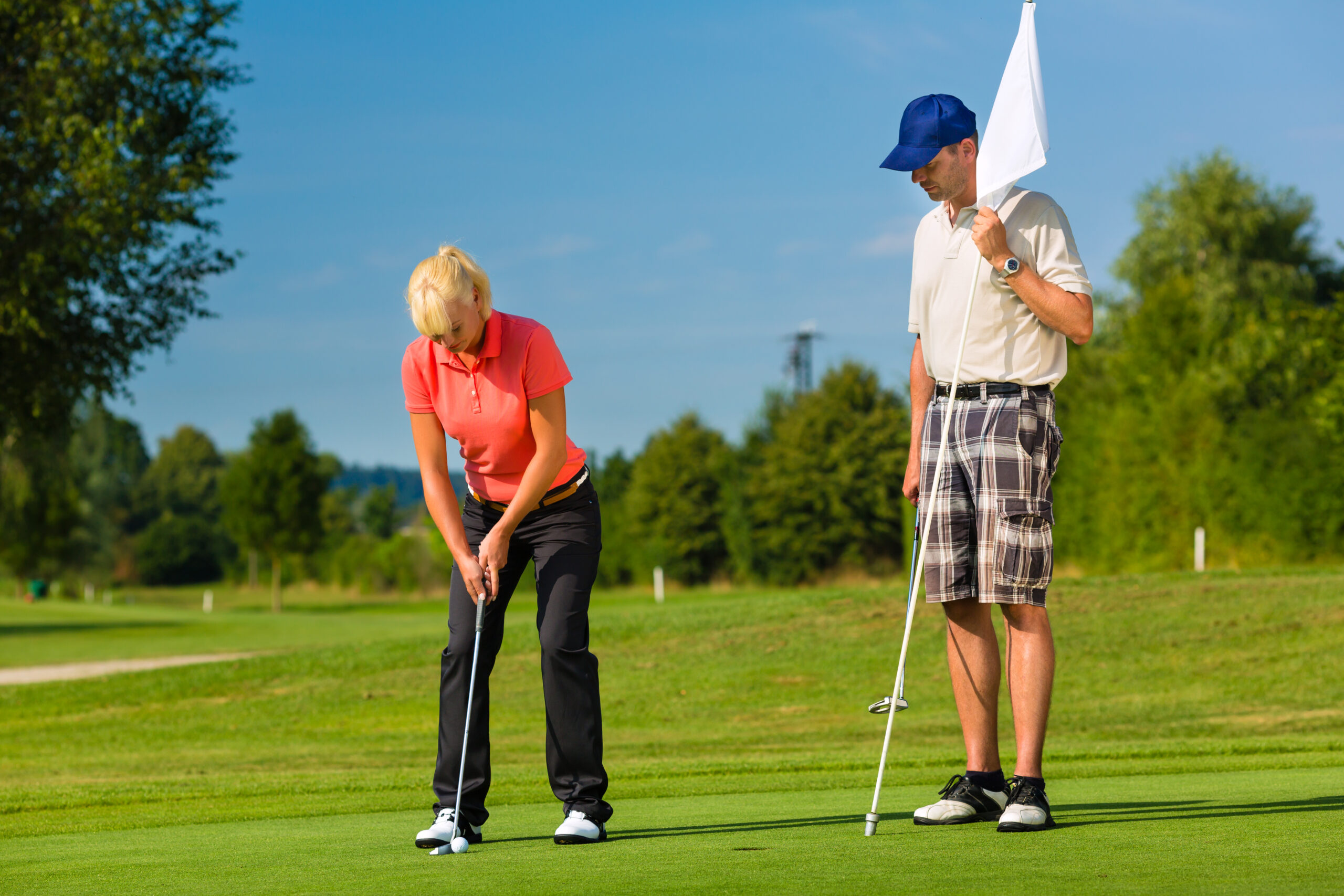 A woman putts a golf ball while a man watches and holds the flag.