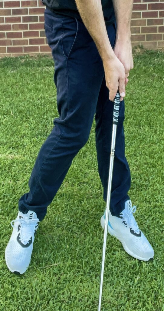 A golfer holds a golf club to demonstrate the proper impact position for the golf swing.