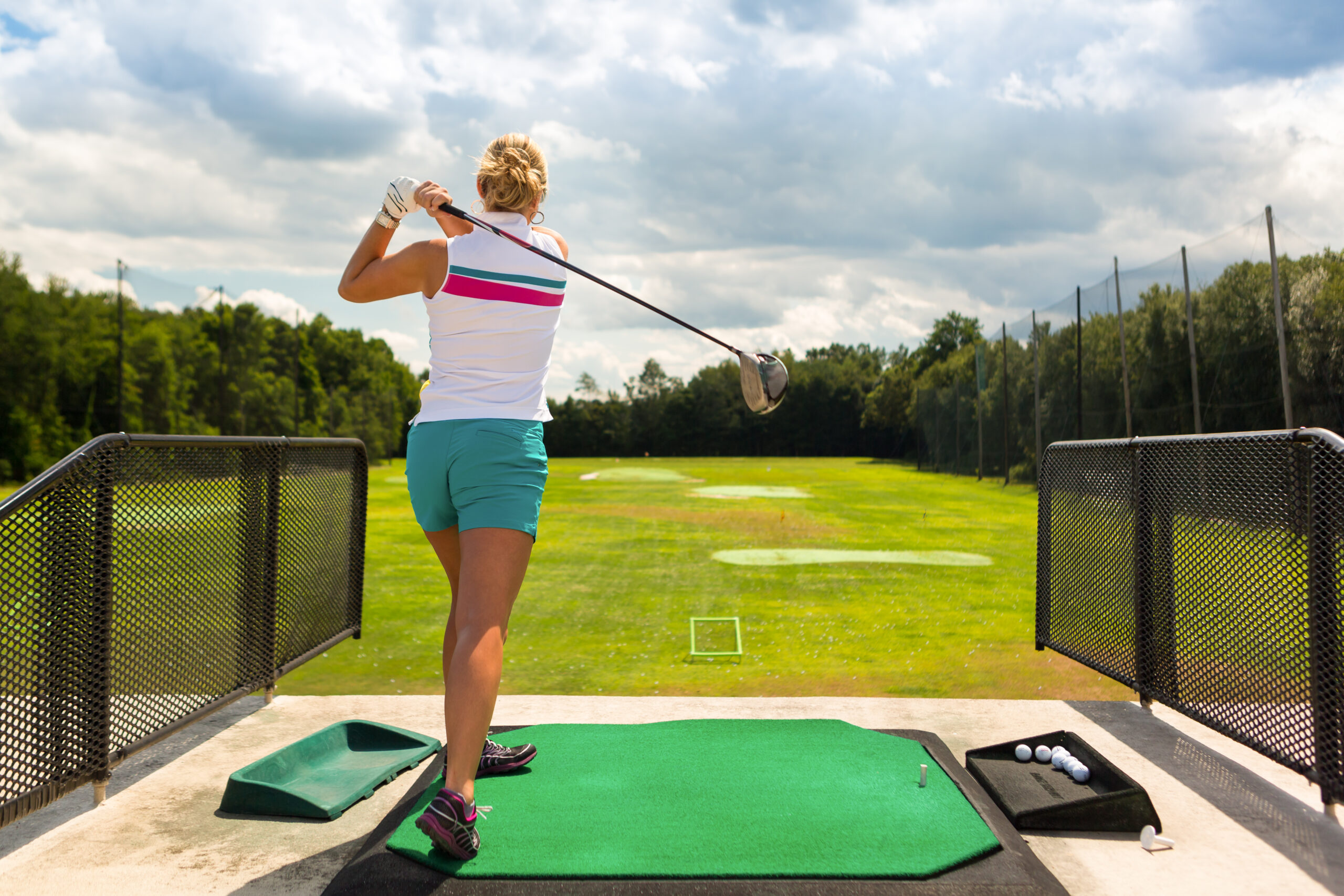 A woman practices her golf swing on the driving range, viewed from behind.