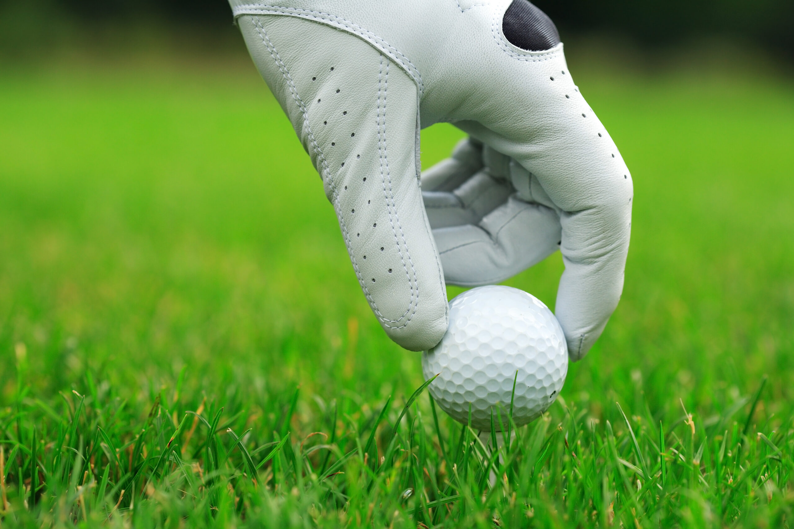 A golf glove is on a hand teeing up a golf ball.