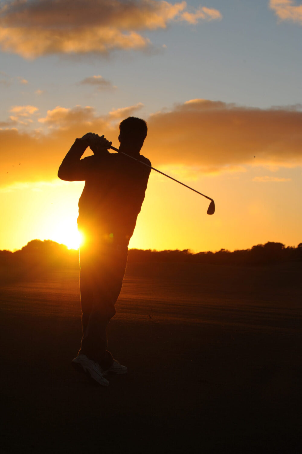 A golfer hitting a golf shot at sunrise.