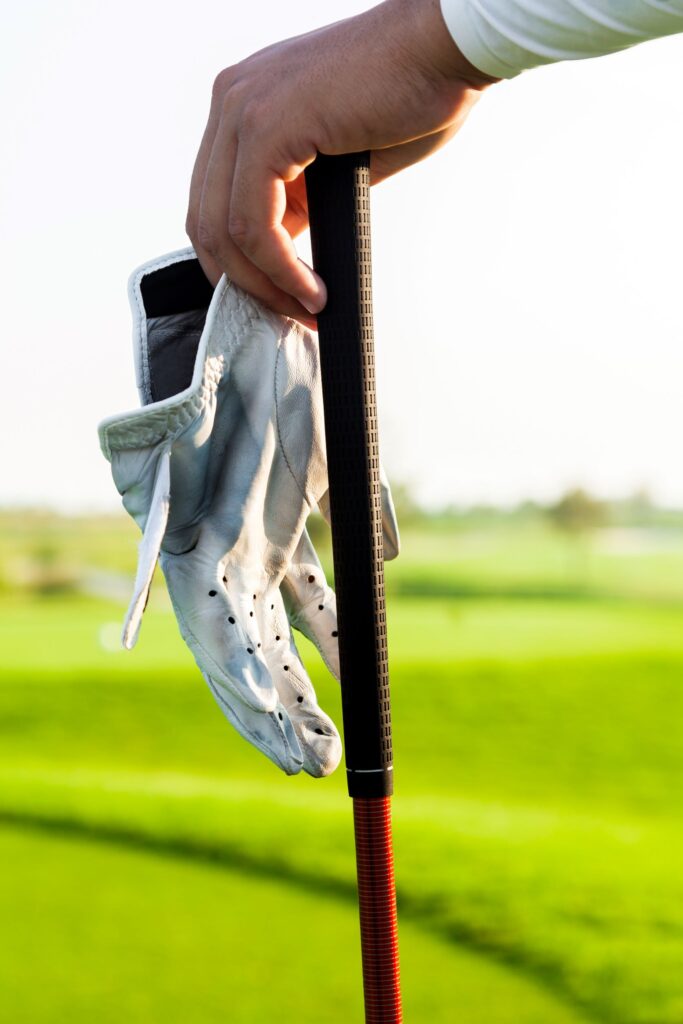 Golfer resting their hand on a golf club while holding a golf glove. 