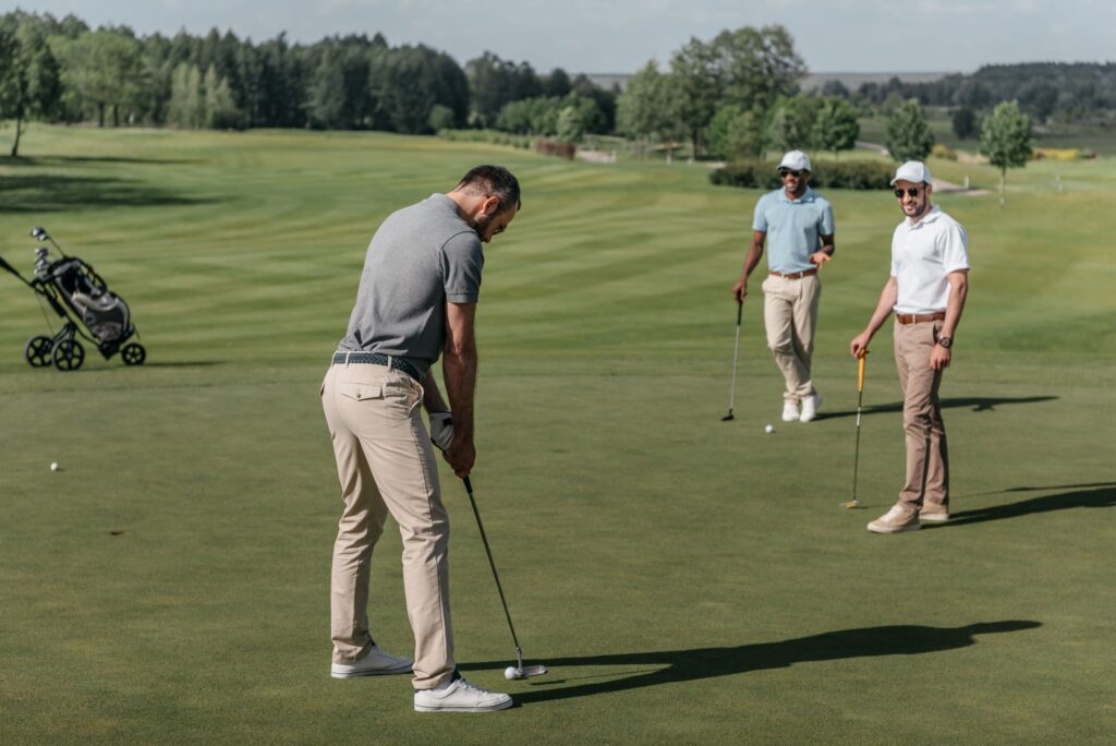 A golfer putts on a golf course while other golfers watch during a match.
