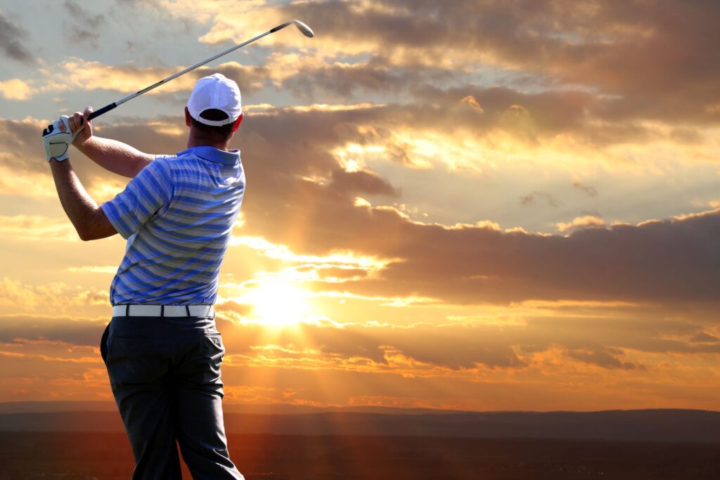 A golfer hits a golf shot at sunrise. 