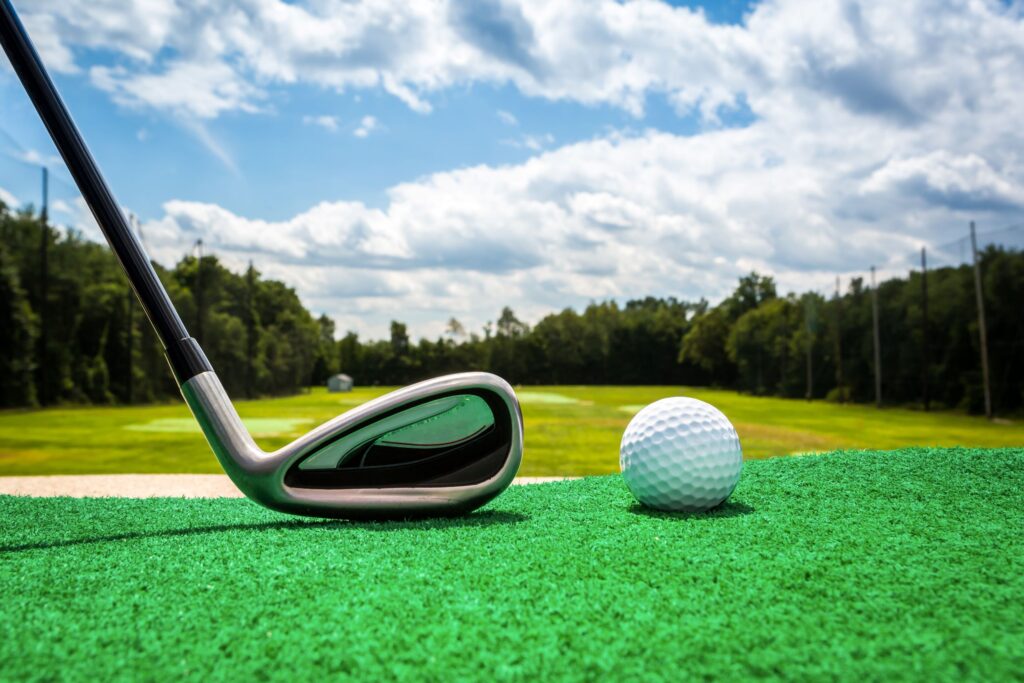 A golf iron and a golf ball with a driving range in the background. 