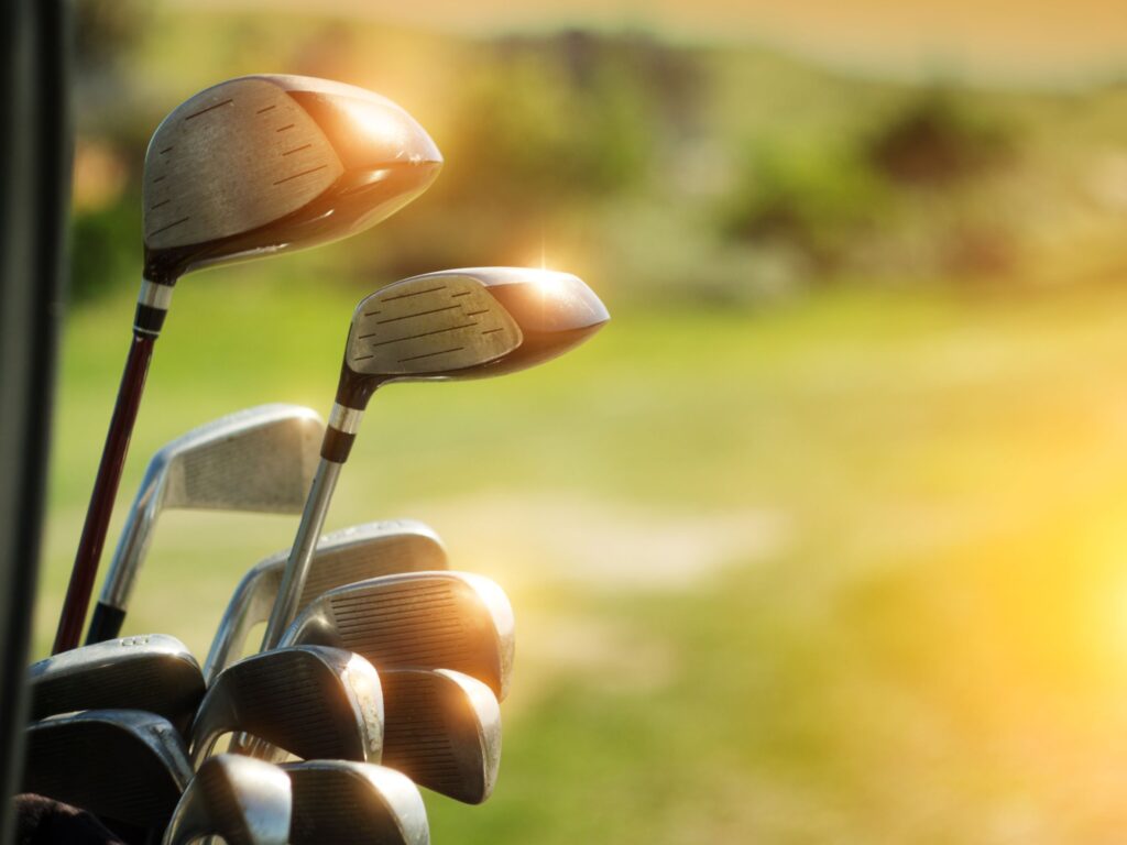 A set of golf clubs organized in a golf bag and setting in the sun. 
