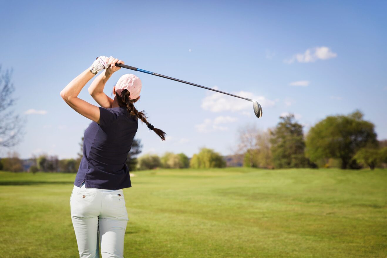 A female golfer hitting a drive on a golf course.