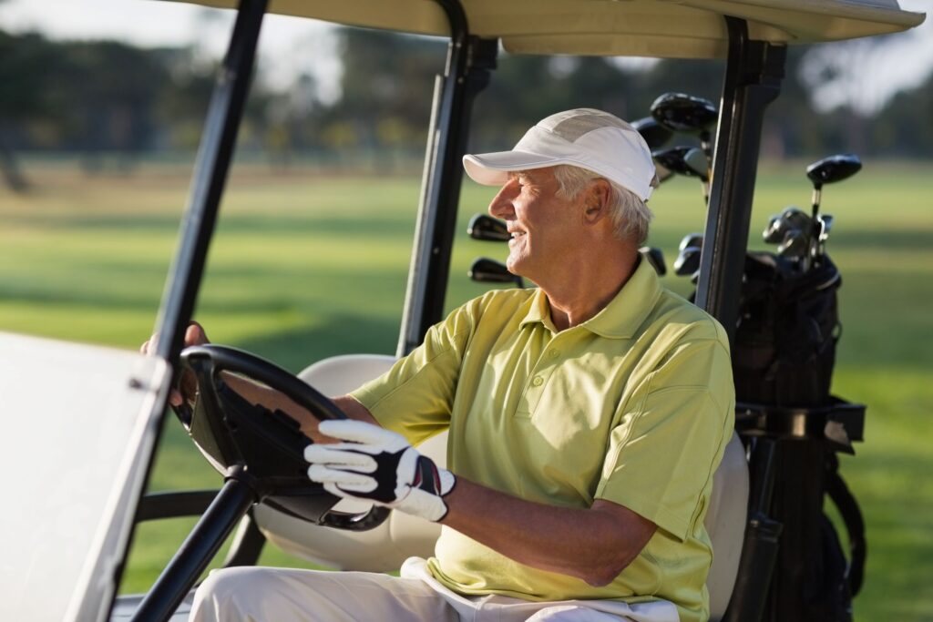 A man playing golf in a cart with his golf clubs.