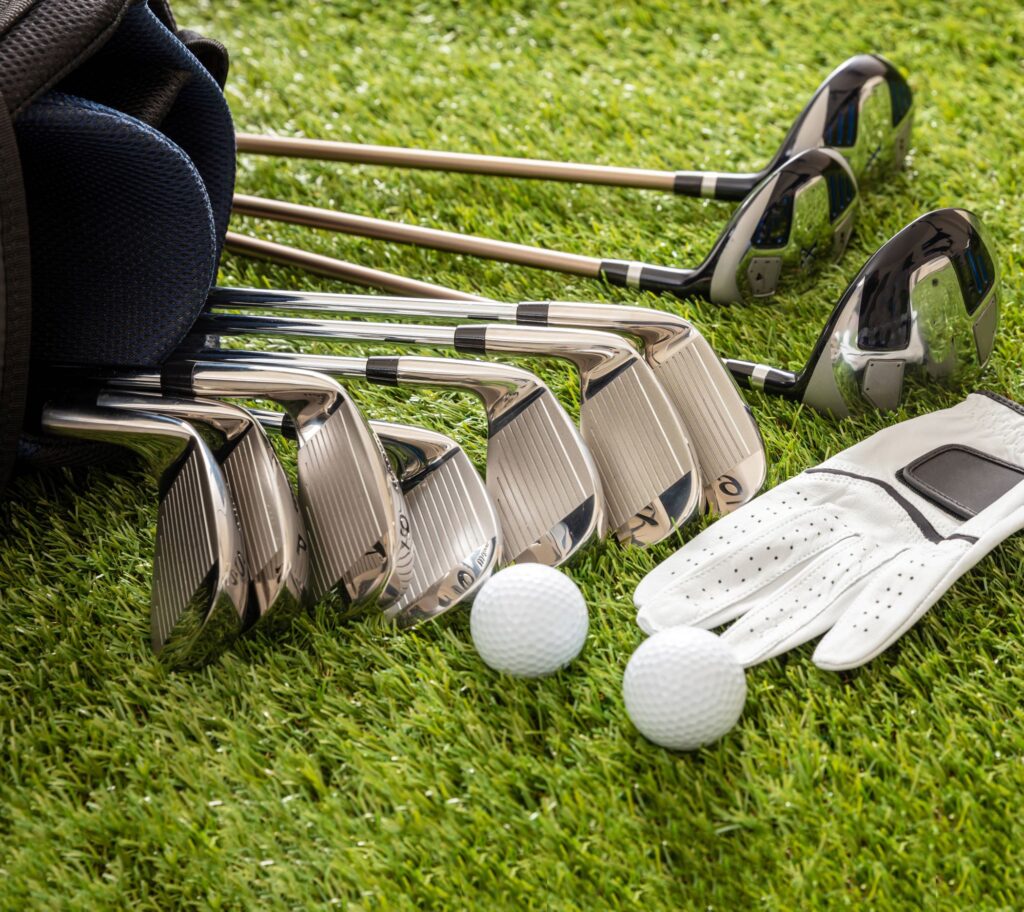 A set of golf clubs lays in the grass with a couple of golf balls and a glove nearby. 