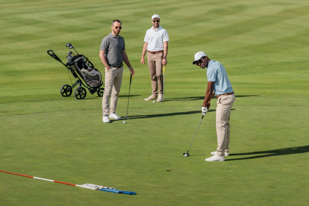 A golfer strokes a putt as his two playing partners watch during a round of golf. 