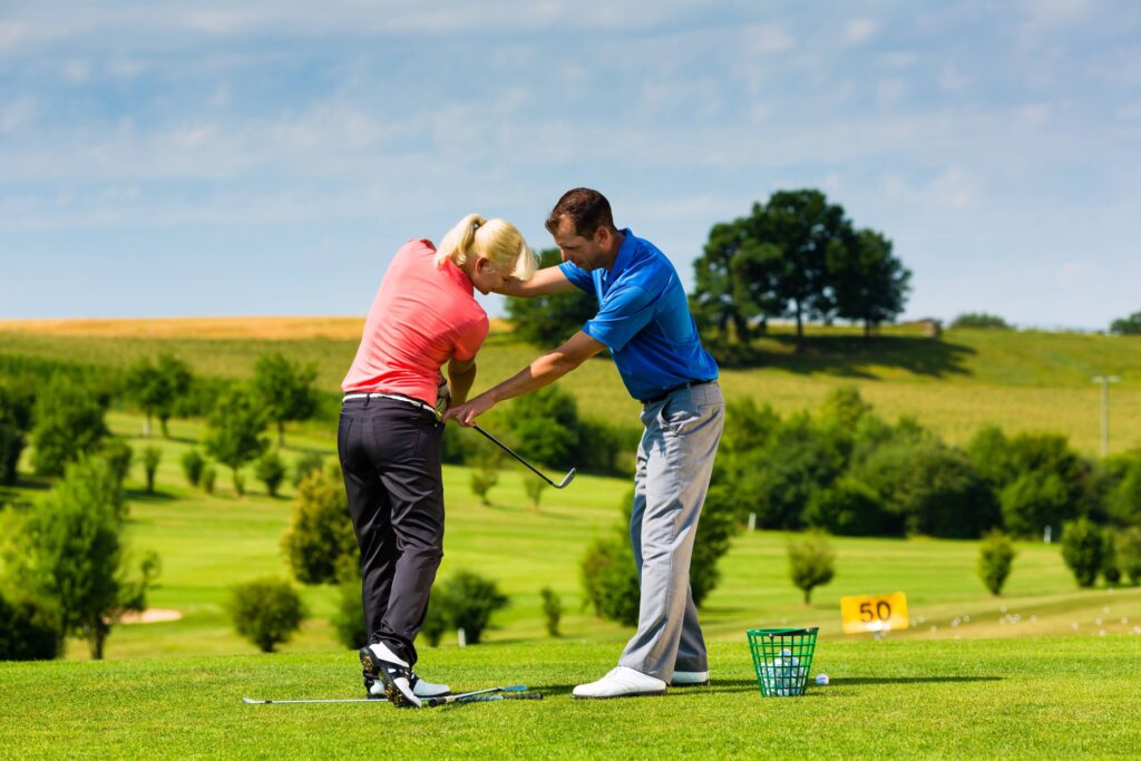 A female golfer receives a golf lesson on a driving range from a professional instructor. 