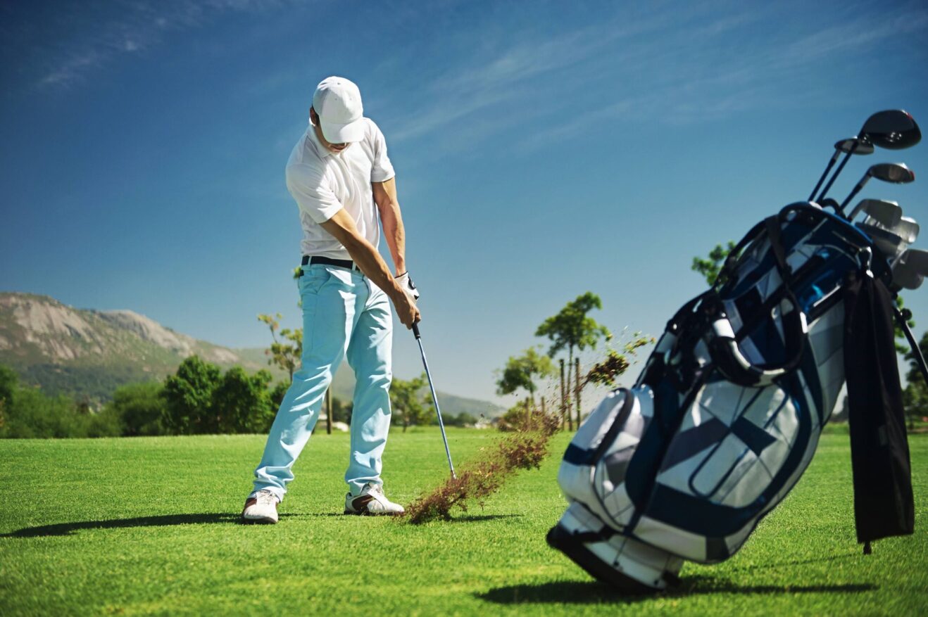 A golfer hits a shot on the course next to his golf bag.