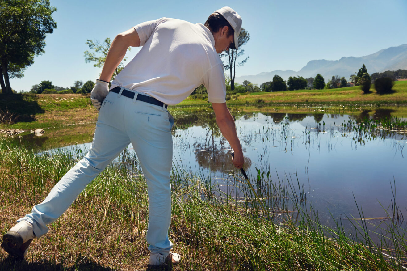 A golfer looking for their golf ball around a water hazard.