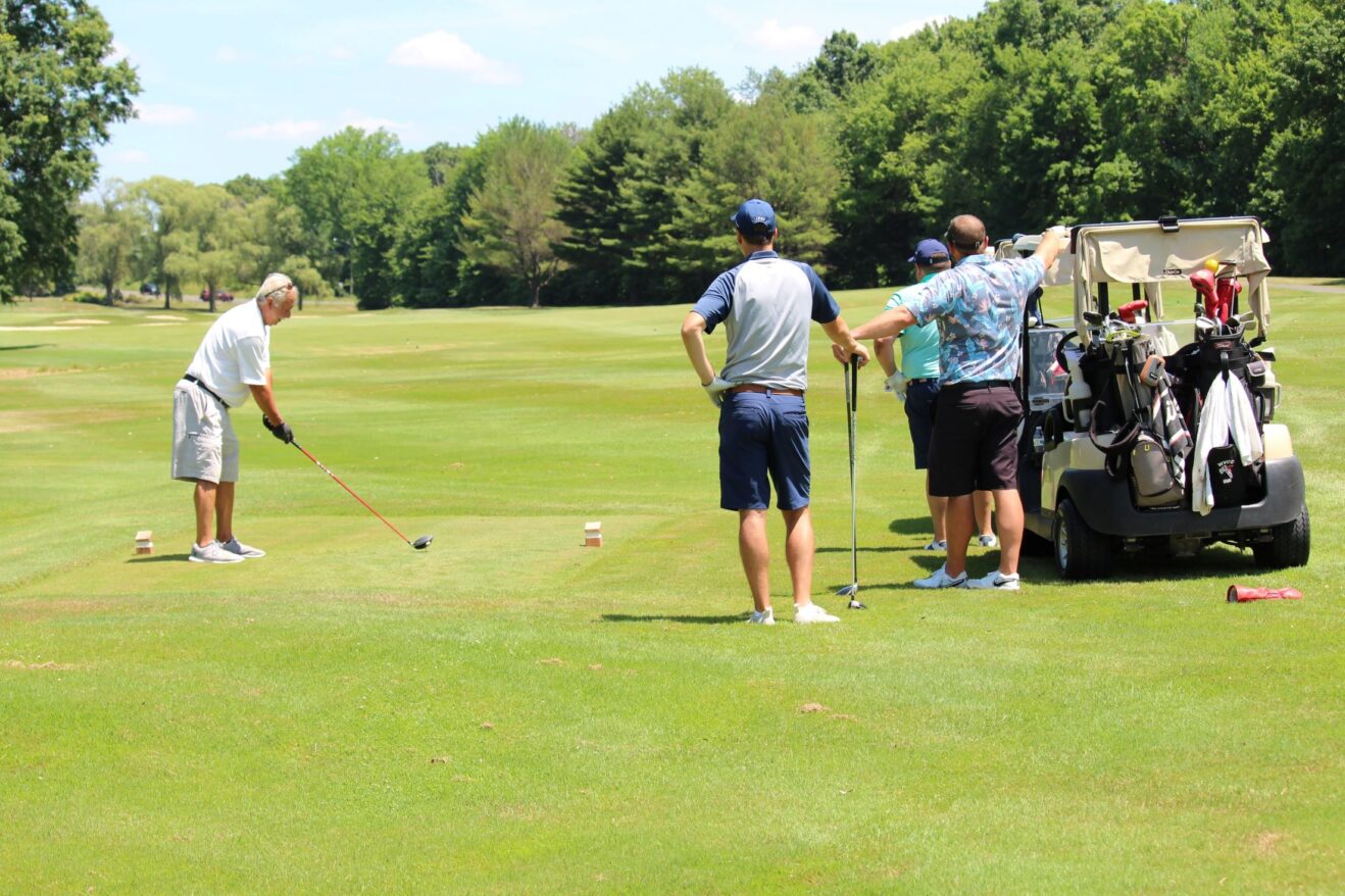 A male golfer tees off on a golf course as other golfers watch.