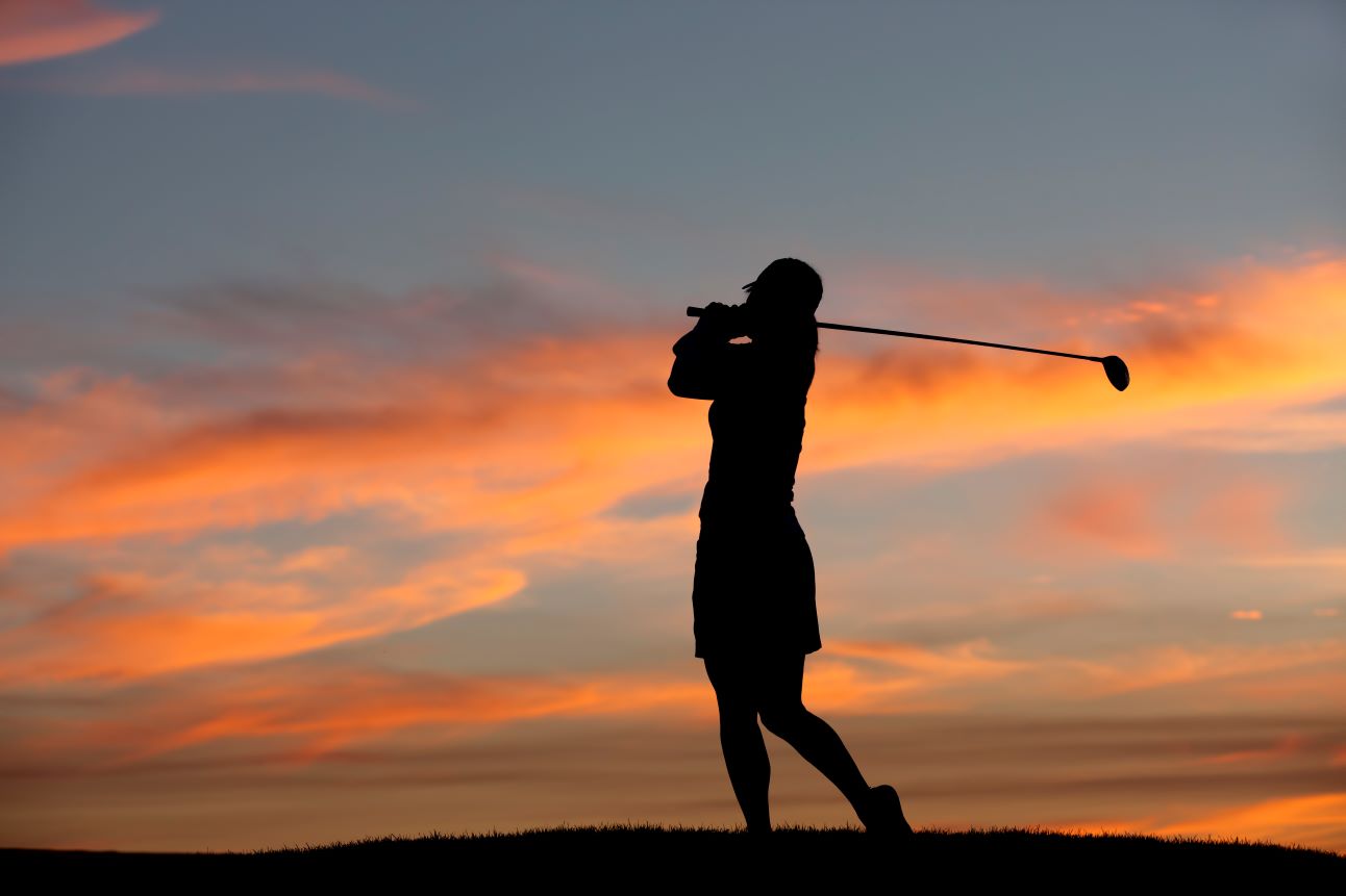 A female golfer hits a shot at sunset.