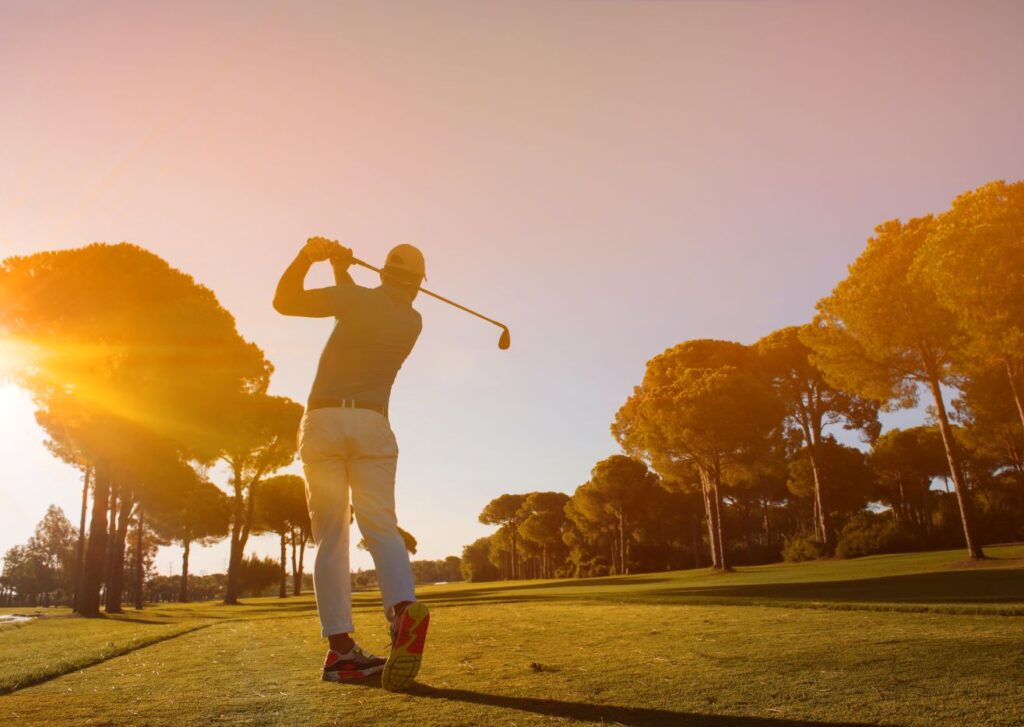 A golfer hits a shot at sunrise.