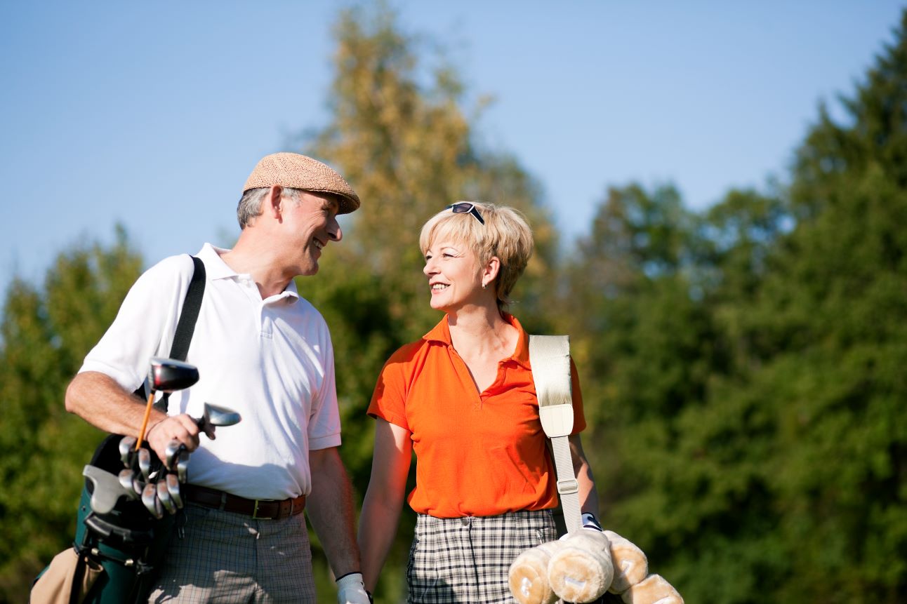 A senior couple walks a golf course during a round.