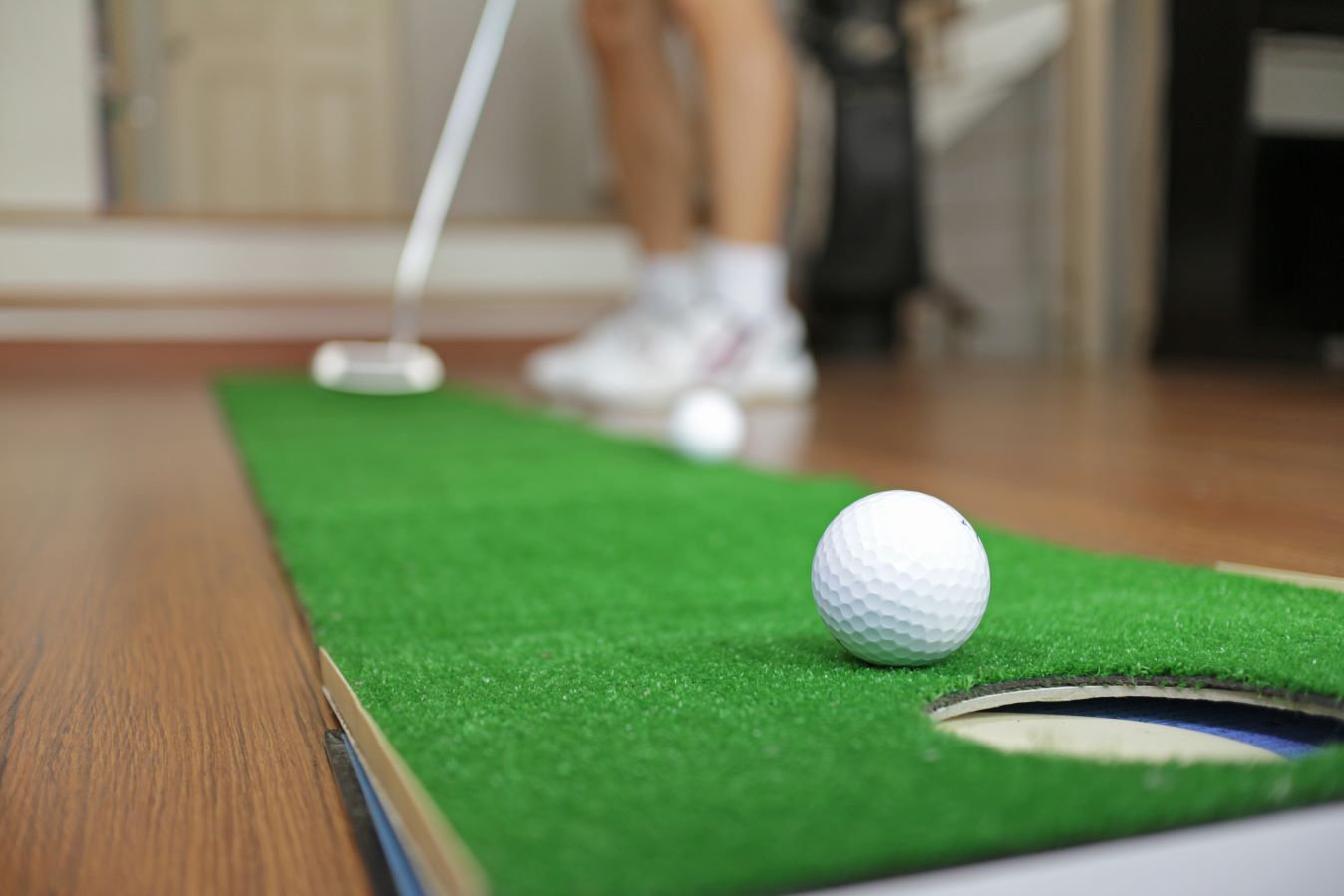 A golfer using a putting mat to practice golf at home.