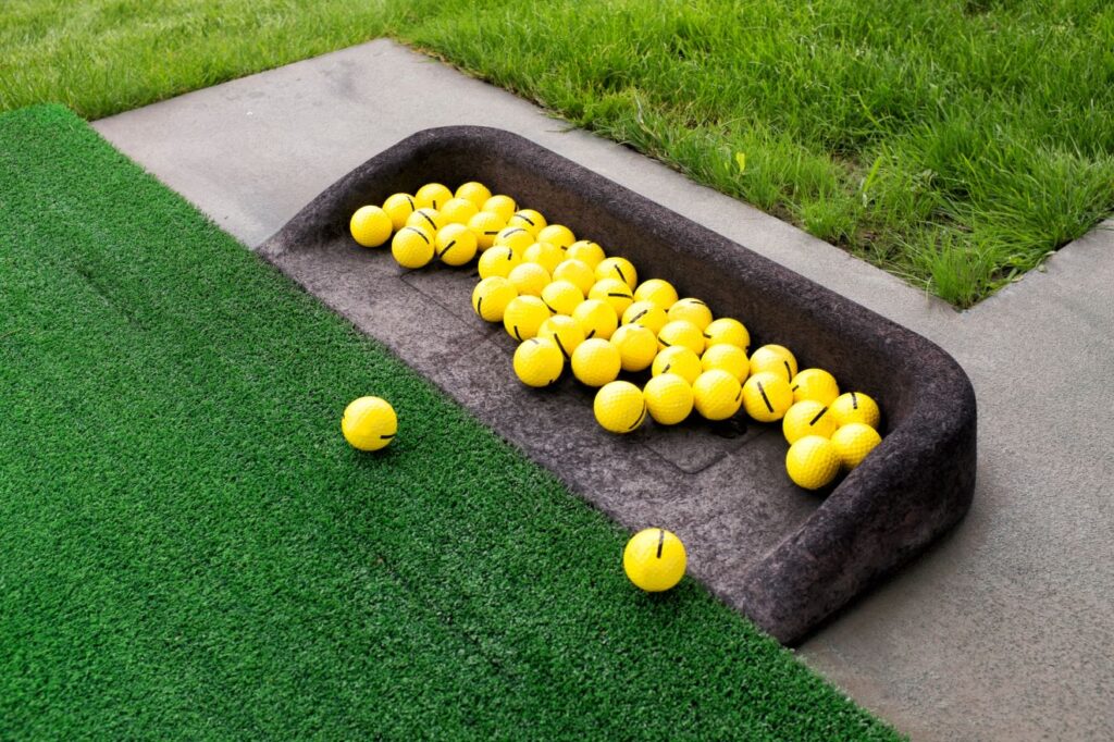A collection of yellow golf balls sitting next to artificial turf. 